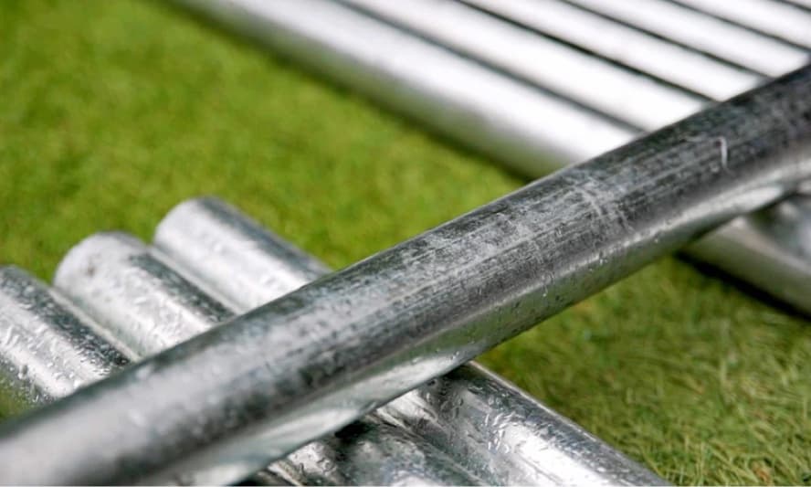 Primer plano de una tubería de acero galvanizado con gotas de agua sobre su superficie, enfatizando la durabilidad y resistencia del material ante condiciones climáticas adversas.