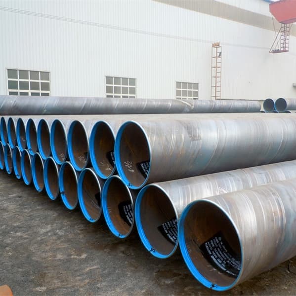 Tubos de acero apilados en frente de un almacén, listos para distribución, resaltando la eficiencia logística y la disponibilidad de producto de MMTubería.