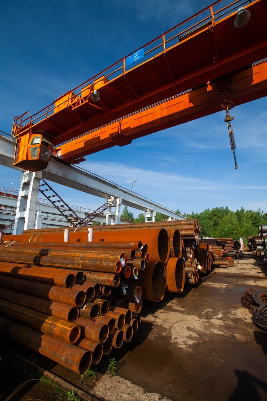 Apilamiento de tuberías de acero en un almacén industrial con grúa, representando la logística eficiente de MMTubería en el manejo y distribución de productos a gran escala.