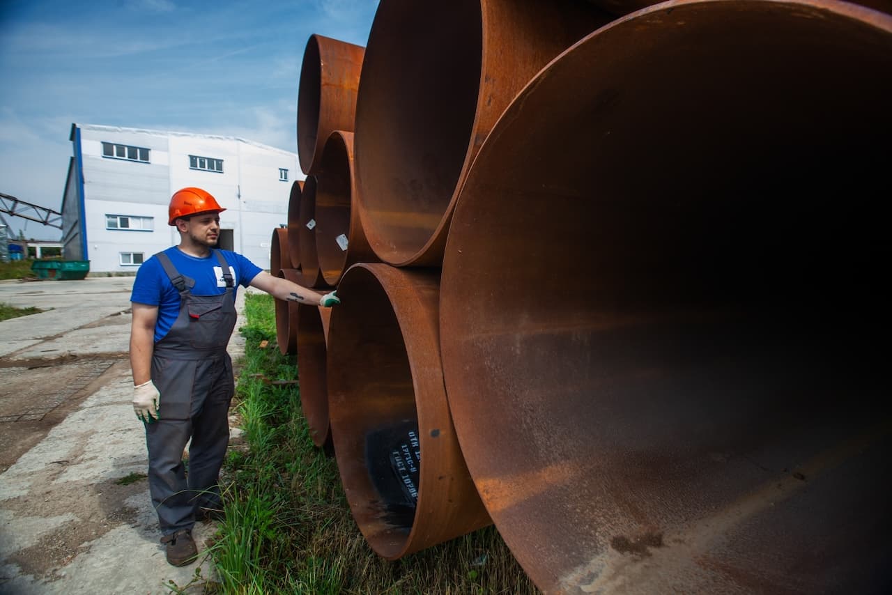 Trabajador inspeccionando grandes tuberías de acero en una fábrica al aire libre, destacando la alta durabilidad y resistencia de las tuberías fabricadas por MMTubería para proyectos industriales.